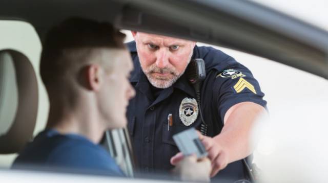 Police officer checking driver's license at a traffic stop through car window.