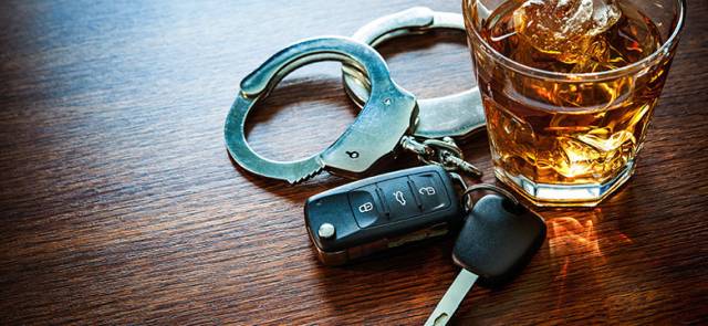 Glass of whiskey, car keys, and handcuffs on a wooden table symbolizing DUI consequences and awareness.
