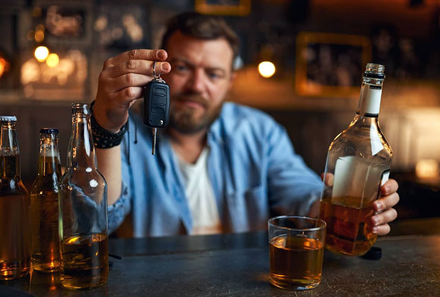 Man in bar holding car keys and whiskey bottle, highlighting drink and drive risk.