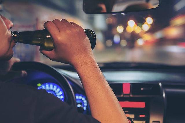 Person drinking beer while driving a car at night, highlighting dangers of drunk driving and road safety concerns.