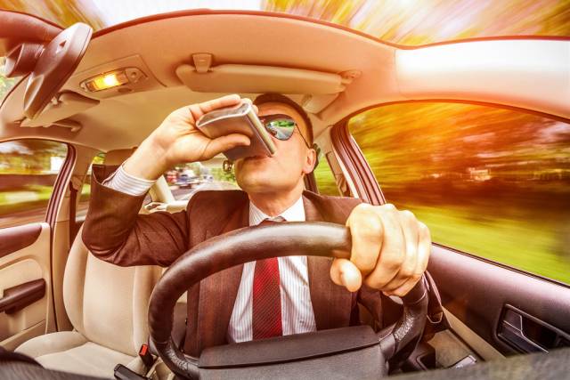 Man in car drinking from flask while driving fast, emphasizing unsafe driving and distracted behavior.