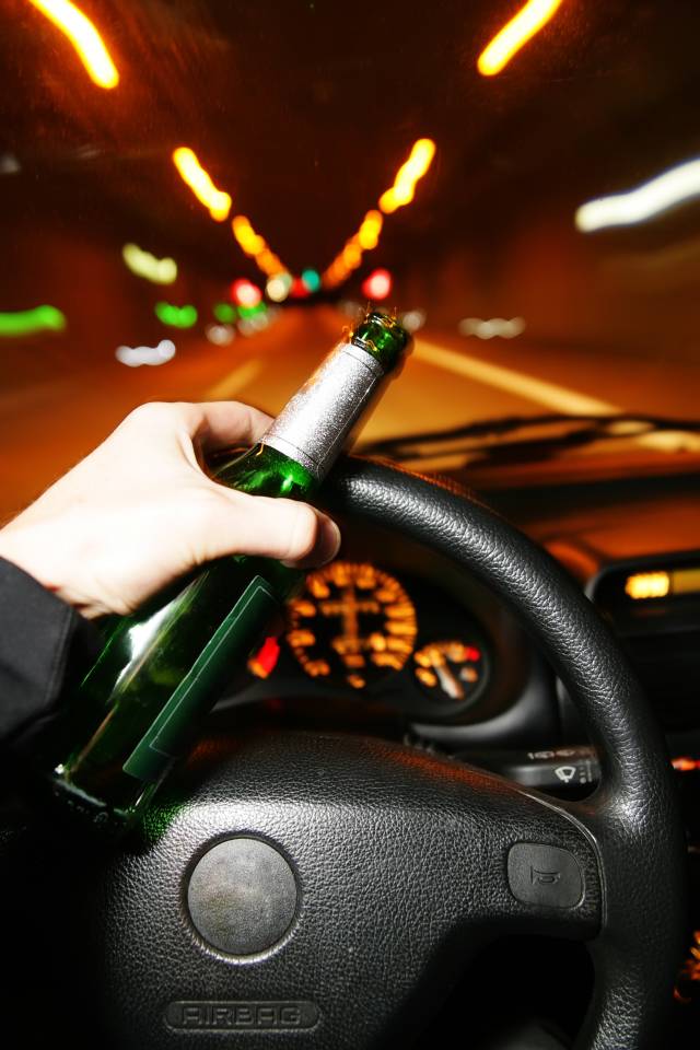 Driving with a beer bottle in hand, blurred tunnel lights in view, highlighting danger of drinking and driving.