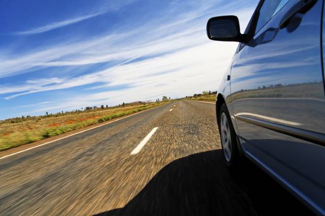 Car driving on an open road under a clear blue sky, showcasing freedom and travel adventure.