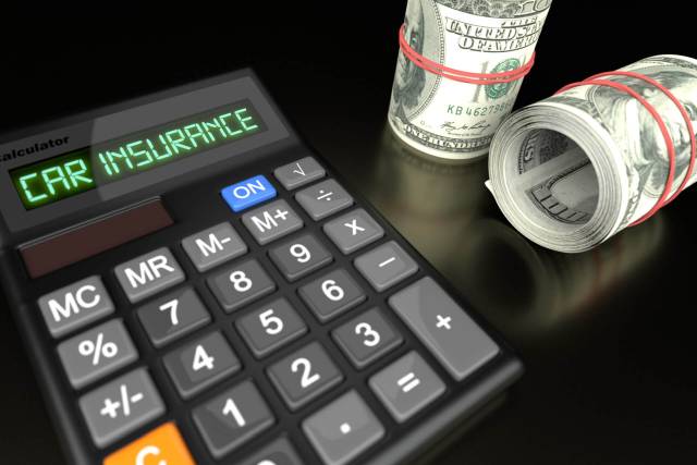Calculator displaying car insurance beside rolled dollar bills on a dark surface.