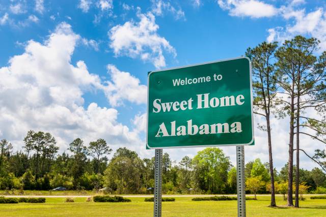 Welcome to Sweet Home Alabama sign with trees and blue sky in the background.