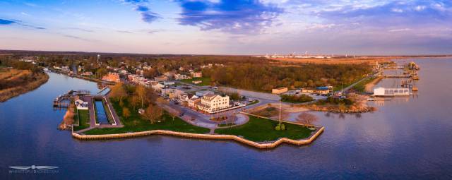 Aerial view of a scenic riverside town at sunset, showcasing houses, green areas, and a serene waterfront.