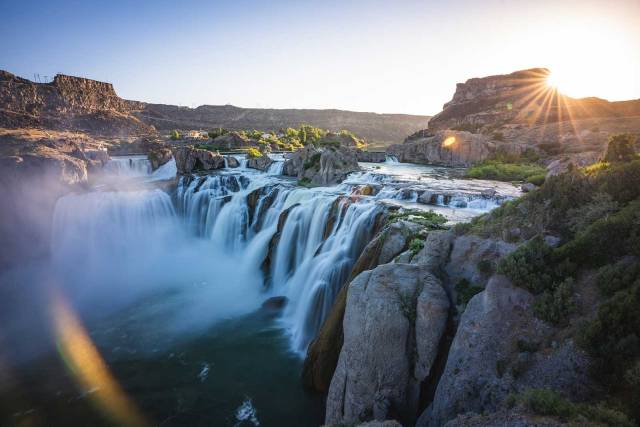Scenic waterfall at Shoshone Falls with sunrise, cascading water, and rugged cliffs in a serene natural setting.