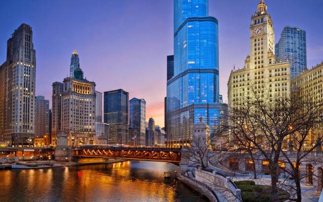 Chicago skyline at dusk with illuminated skyscrapers and river, featuring iconic architectural landmarks.
