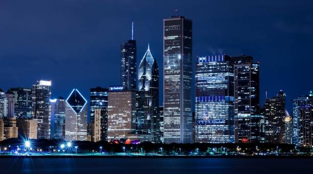 Chicago skyline at night with illuminated skyscrapers reflected on Lake Michigan.