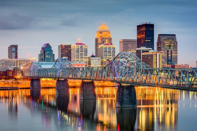 Skyline of Louisville, Kentucky at dusk with illuminated bridge reflecting on the Ohio River.