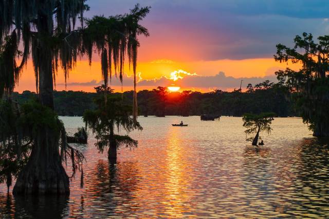 Sunset over a tranquil lake with trees and a canoe, creating a serene outdoor scene.