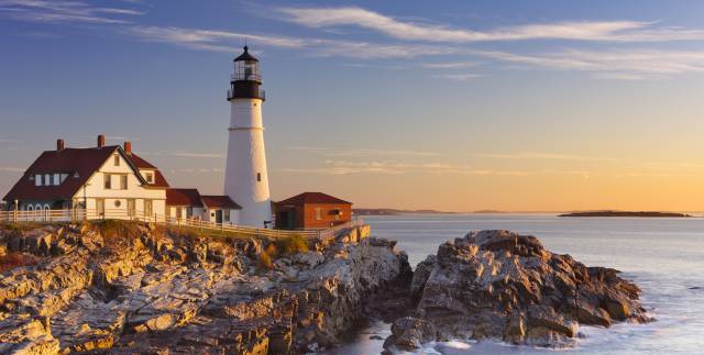 Lighthouse at sunset on rocky coast, overlooking ocean with a calm sky. Scenic view for travel and nature inspiration.