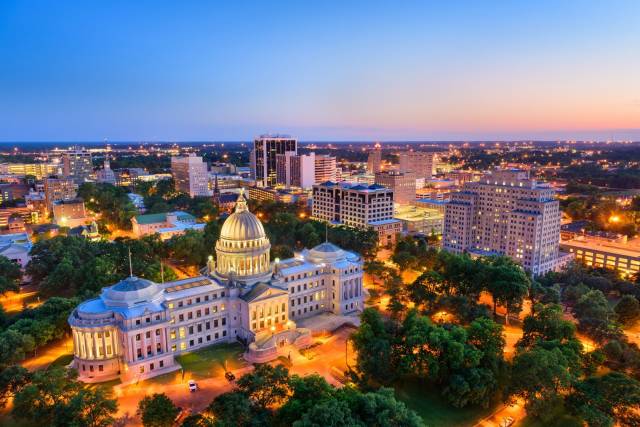 Aerial view of Jackson, Mississippi skyline at sunset with the illuminated state capitol building in the foreground.