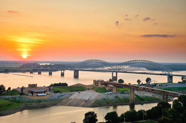 Sunset view of a bridge over the Mississippi River with vibrant orange skies and calm waters.