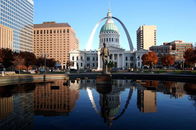 Historic courthouse and Gateway Arch reflected in water, St. Louis cityscape under clear blue sky.