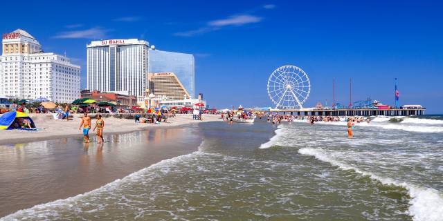 Beachfront with lively crowds, Ferris wheel, and hotel skyline under clear blue sky.