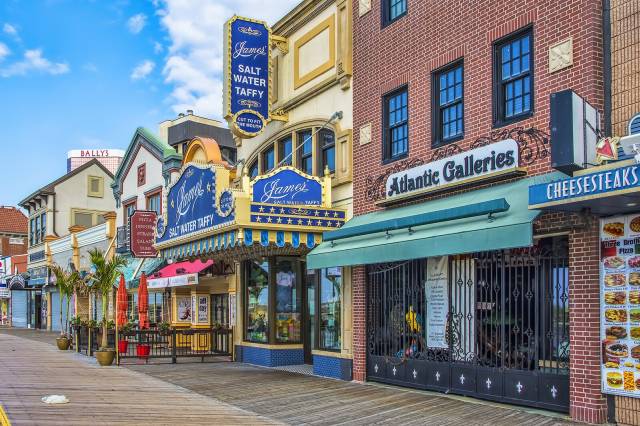 Colorful shops along a vibrant boardwalk, featuring saltwater taffy and dining options, under a clear blue sky.