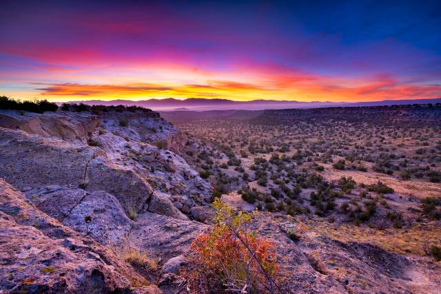 Vibrant sunset over a rocky desert landscape, with colorful sky and distant mountains, creating a serene natural scene.
