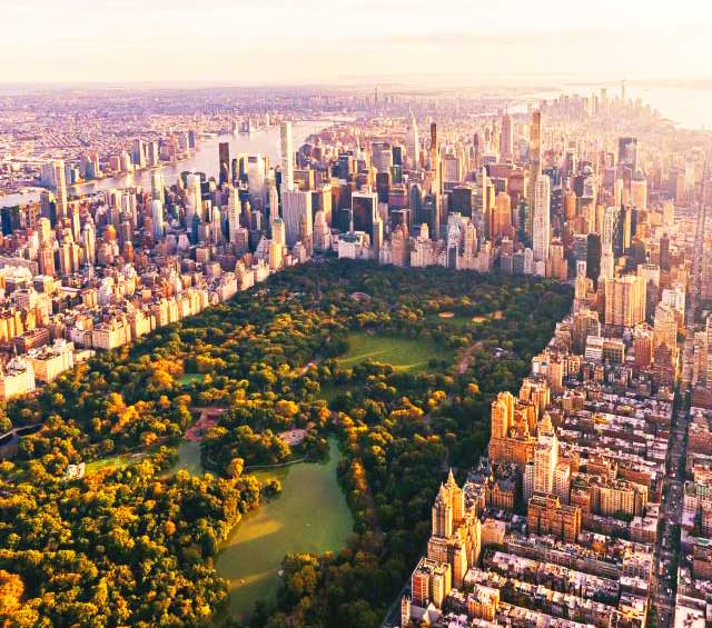 Aerial view of Central Park and Manhattan skyline at sunset, highlighting lush greenery and urban architecture.