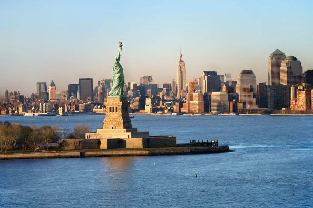 Statue of Liberty overlooking New York City skyline with clear skies.