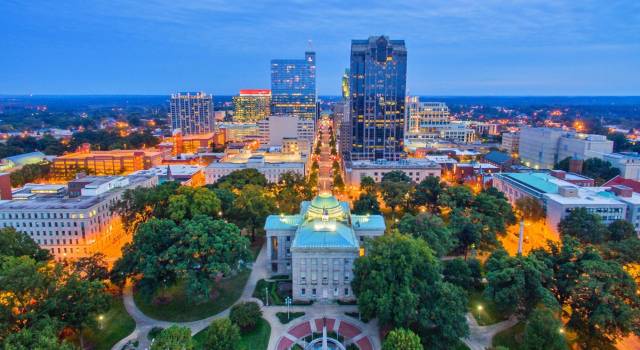 Downtown Raleigh skyline at dusk, highlighting the cityscape with illuminated buildings and lush greenery.