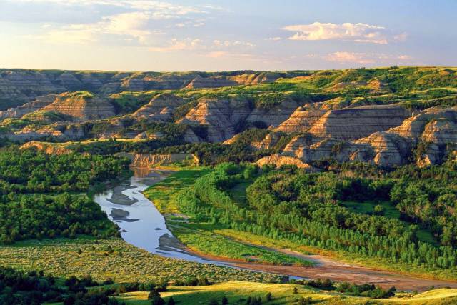 Scenic view of lush green valley and river winding through rugged hills under a blue sky with scattered clouds.