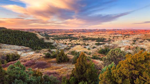 Scenic view of sunset over a vast landscape with rolling hills, colorful sky, and lush greenery.