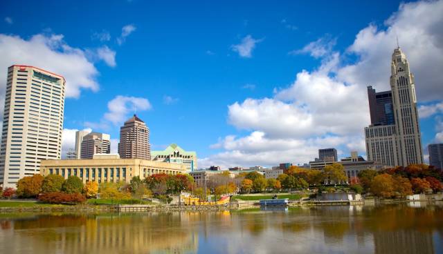 Skyline of Columbus, Ohio with skyscrapers and river reflecting a sunny autumn day under a blue sky with clouds.