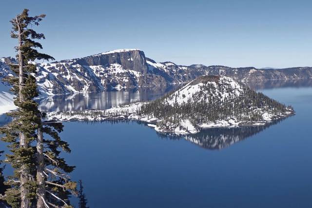 Scenic view of Crater Lake with snow-covered Wizard Island and clear blue sky in Oregon's national park.