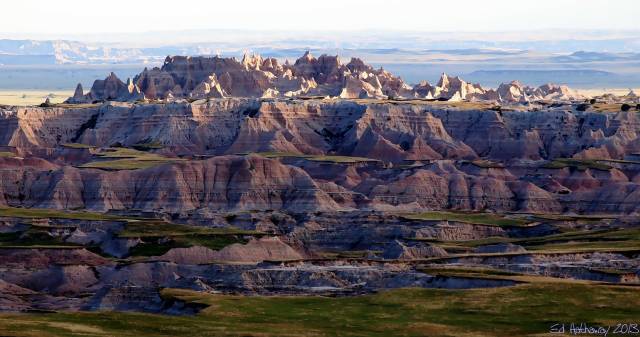 Rugged Badlands landscape with layered rock formations and green grassy patches under a clear sky.