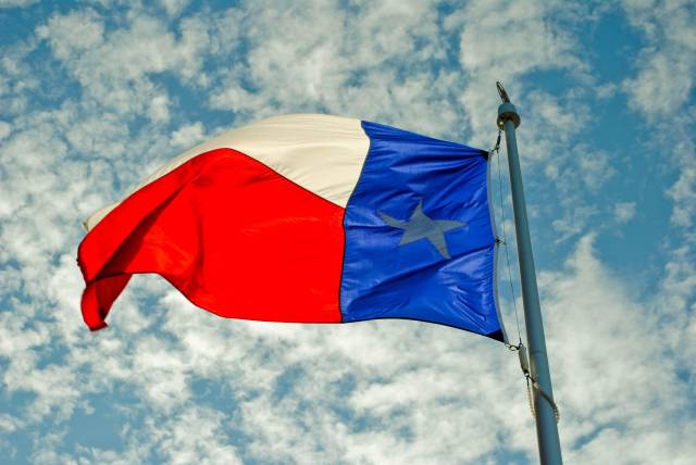 Texas flag waving against a cloudy sky, showcasing red, white, and blue colors with a single star.
