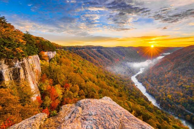 Sunrise over a vibrant autumn landscape with river and cliffs in New River Gorge National Park, West Virginia.
